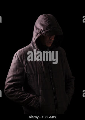 Scary and creepy man hiding in the shadows, standing in the darkness / black background hood hiding face shadows dangerous mysterious stalker hood Stock Photo