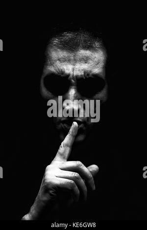 Angry mature man with aggressive look making silence sign in threatening and creepy way. Black background / shh shhh shut up scary creepy angry secret Stock Photo