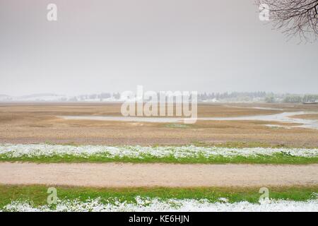 Straight  muddy tractor way. April weather. Wet spring snow in already fresh green meadows bellow mountains. Stock Photo