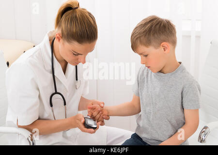 Female Doctor Examining Blood Sugar Of Little Boy With Glucometer Stock Photo