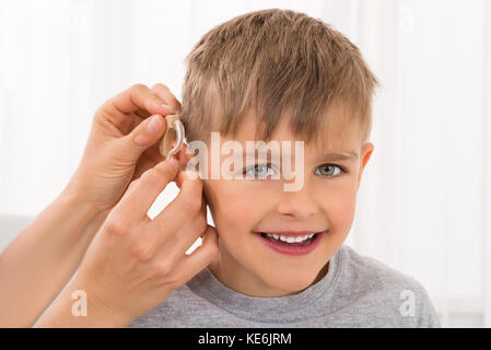 Close-up Of A Doctor Fitting Hearing Aid On Smiling Boy's Ear Stock Photo