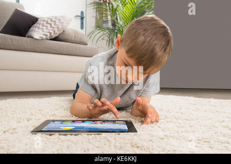 Boy Lying On Carpet Using Digital Tablet With Multicolored Apps On It Stock Photo