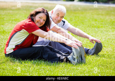 Elderly Senior Couple Doing Stretching Exercise In Park Stock Photo