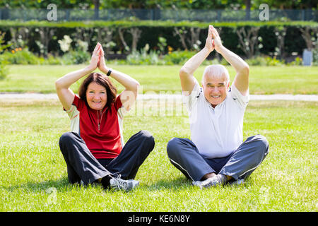 Happy Senior Couple Practising Yoga In Park Stock Photo