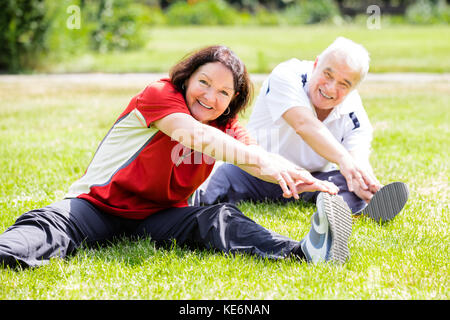 Smiling Senior Couple Doing Fitness Exercise In Park Stock Photo