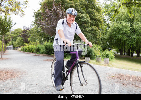 Smiling Senior Man Riding Bicycle In Park Stock Photo