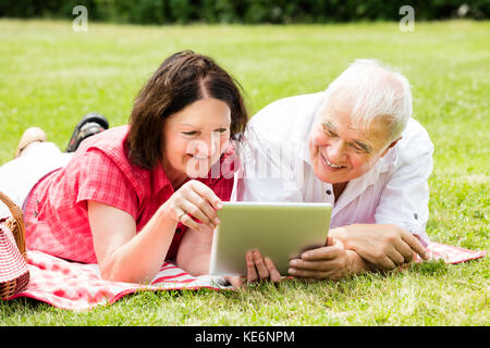 Happy Senior Couple Using Digital Tablet In Park Stock Photo