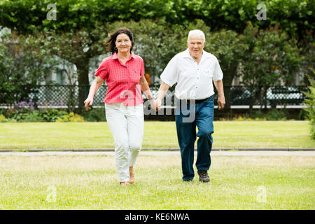 Happy Senior Couple Running In Park Holding Hands Stock Photo