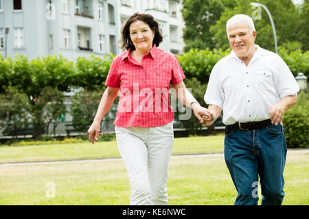 Happy Senior Couple Running In Park Holding Hands Stock Photo