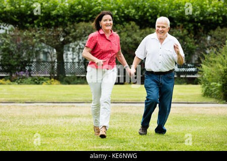 Happy Senior Couple Running In Park Holding Hands Stock Photo