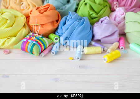 Colored fabric folded in the form of rose flowers. Scissors, tape measure, needle, needle bar, buttons. Stock Photo