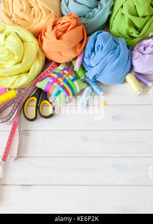 Colored fabric folded in the form of rose flowers. Scissors, tape measure, needle, needle bar, buttons. Stock Photo