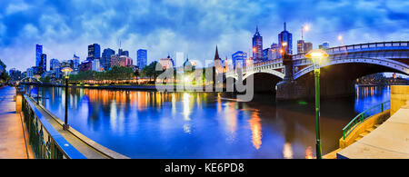 Princes bridge across Yarra river to Flinders station and Melbourne CBD dark at sunrise with bright street lights and skyscrapers illumination reflect