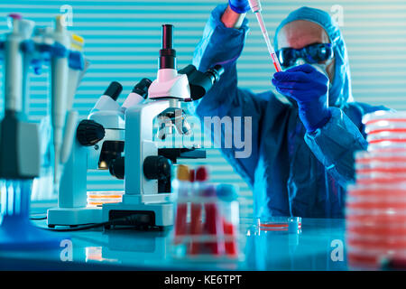 Research Of dangerous viruses in the laboratory. Prevention of a pandemic. A scientist in a biological protective suit works with a pipette Stock Photo