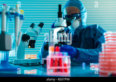 Research Of dangerous viruses in the laboratory. Prevention of a pandemic. A scientist in a biological protective suit works with a pipette Stock Photo