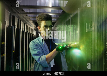 Male IT technician holding glowing futuristic digital tablet in server room Stock Photo