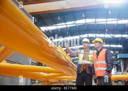 Male foreman with clipboard explaining to worker in factory Stock Photo