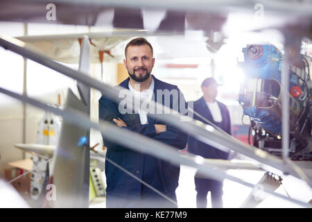 Portrait confident male airplane mechanic standing at airplane in hangar Stock Photo