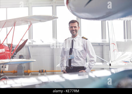 Portrait smiling male pilot standing near airplane in hangar