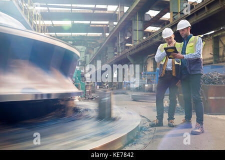 Male foreman and engineer with digital tablet talking in factory Stock Photo