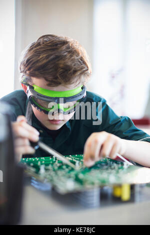 Focused boy student in goggles soldering circuit board in classroom Stock Photo