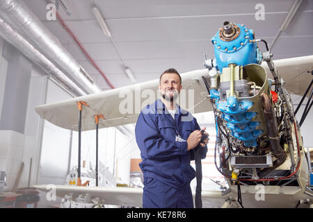 Portrait confident male airplane mechanic working on biplane in hangar Stock Photo