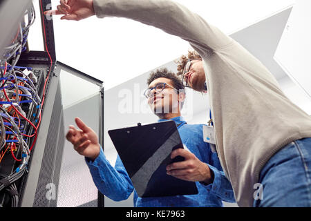 Male IT technicians with clipboard talking at panel in server room Stock Photo