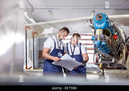 Male engineer mechanics examining plans, fixing airplane in hangar Stock Photo