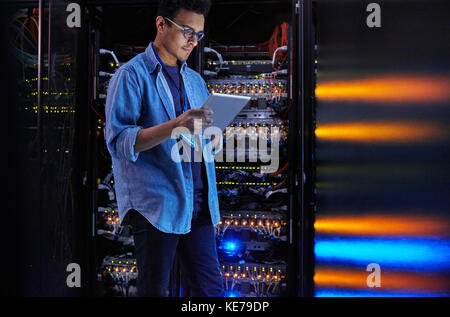 Focused male IT technician using digital tablet at panel in dark server room Stock Photo