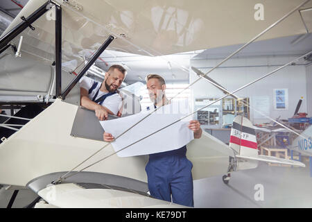 Male engineer mechanics examining plans at airplane in hangar Stock Photo