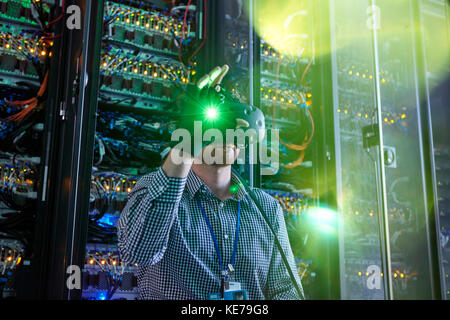 Male computer programmer using virtual reality simulator glasses and glowing glove in server room Stock Photo