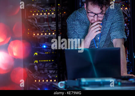 Focused male IT technician working at laptop in dark server room Stock Photo