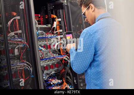 Male IT technician performing diagnostics on panel in server room Stock Photo