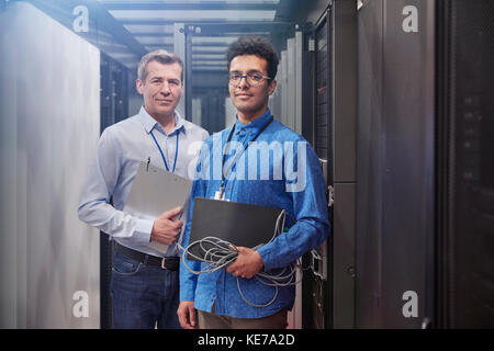 Portrait confident male IT technicians with laptop and clipboard in server room Stock Photo