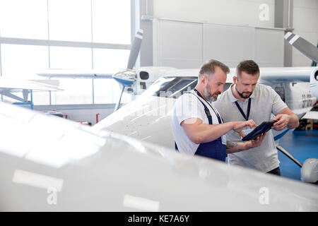 Male mechanic engineers using digital tablet near airplane in hangar Stock Photo