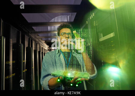 Male IT technician using futuristic digital tablet in dark server room Stock Photo