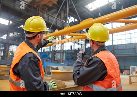 Male workers watching equipment being raised in factory Stock Photo