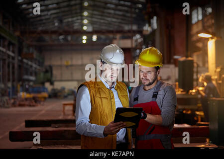 Male foreman and engineer using digital tablet in dark factory Stock Photo