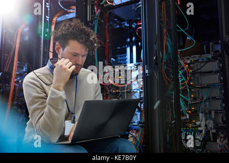 Focused male IT technician using laptop in server room Stock Photo