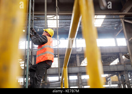 Male worker climbing ladder in factory Stock Photo