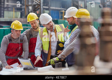 Male foreman, engineers and workers at laptop meeting, discussing blueprints in factory Stock Photo