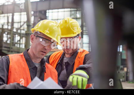 Male workers discussing paperwork in factory Stock Photo