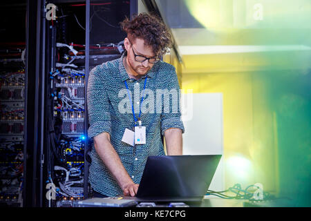 Male IT technician working at laptop in server room Stock Photo