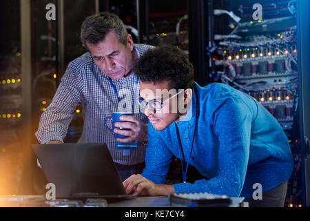 Focused male IT technicians working at laptop in dark server room Stock Photo