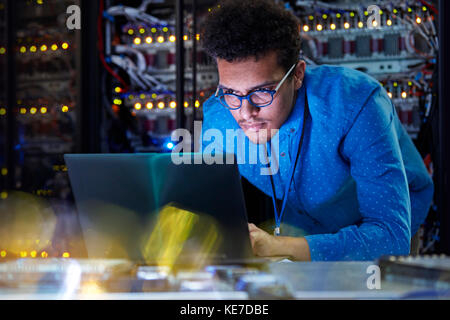 Focused male IT technician working at laptop in dark server room Stock Photo