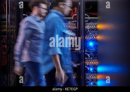 Male IT technicians walking in dark server room Stock Photo