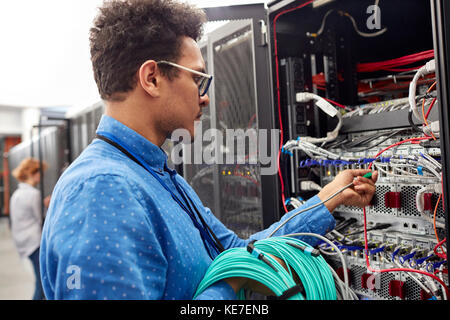 Male IT technician plugging cable into panel in server room Stock Photo