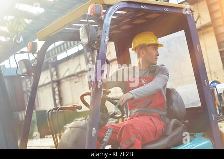 Male worker driving forklift, backing up in factory Stock Photo