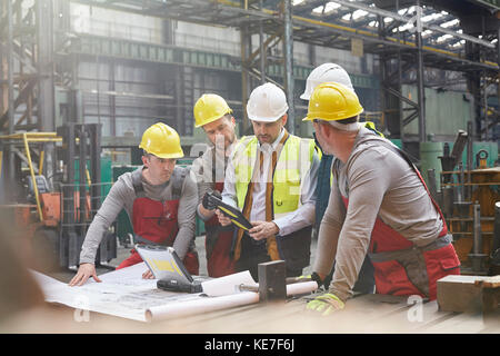 Male foreman, engineers and workers with digital tablet meeting in factory Stock Photo
