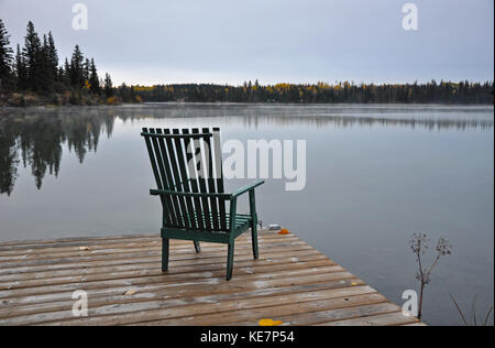 Empty wooden chair on dock on early autumn morning looking out over lake